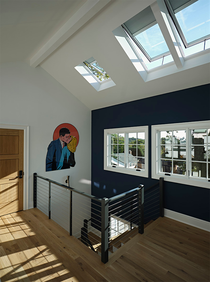 Modern stairwell with multiple skylights bringing in natural light, featuring bold wall art and a sleek railing design